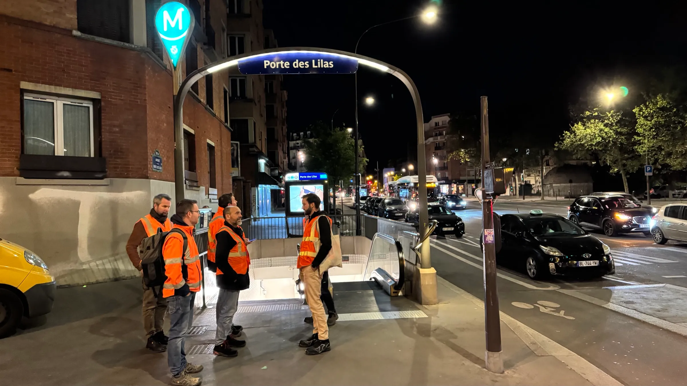 Équipe en gilets orange devant la bouche de métro Porte des Lilas, de nuit